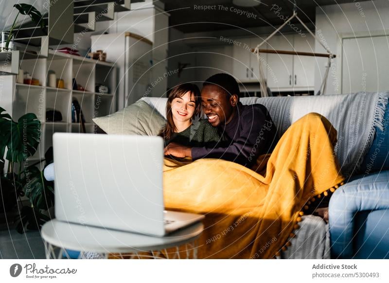 Content diverse couple watching movie on laptop cuddle together relationship blanket hug home multiracial multiethnic sofa love weekend happy girlfriend relax