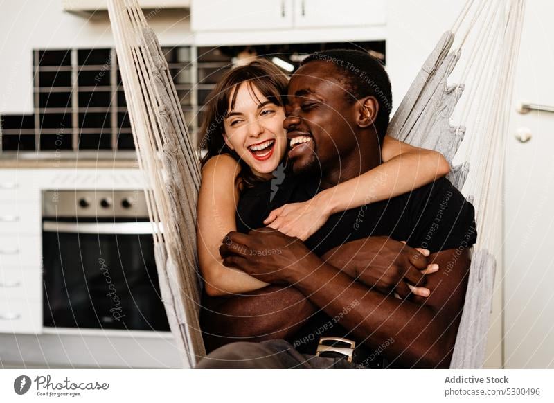 Happy multiethnic couple hugging on swing chair laugh together cuddle kitchen weekend cheerful happy chill relax multiracial diverse relationship embrace love