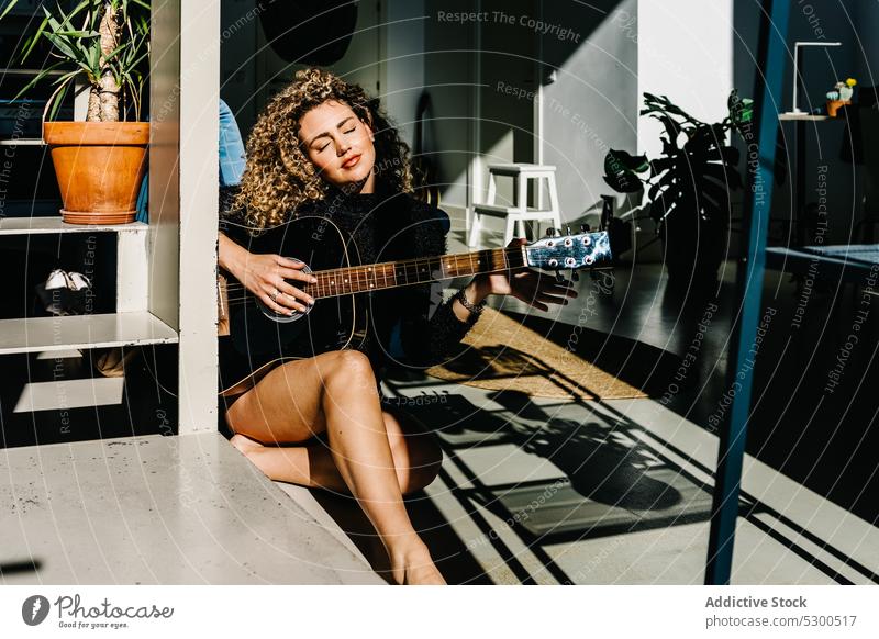 Focused woman playing guitar on floor music musician instrument guitarist practice window hobby acoustic female young melody talent sound home concentrate song