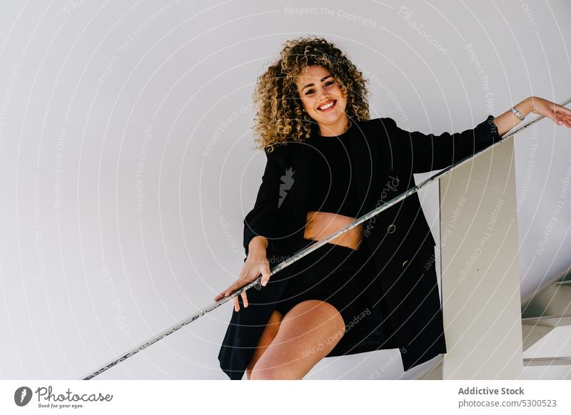 Cheerful woman leaning on railing smile curly hair style positive trendy happy rest outfit cheerful modern female young fashion optimist appearance confident