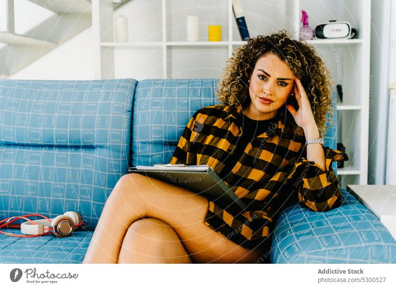 Smiling woman writing notes in clipboard take note write at home sofa weekend imagination thought compose smile female young curly hair checkered shirt casual