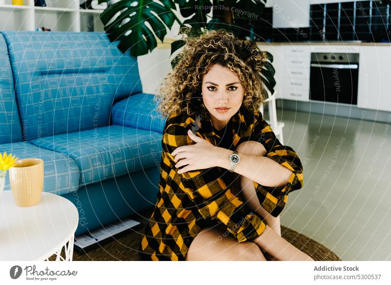 Alluring woman in checkered shirt looking at camera sensual model style sofa curly hair floor fashion portrait appearance female young comfort home relax casual