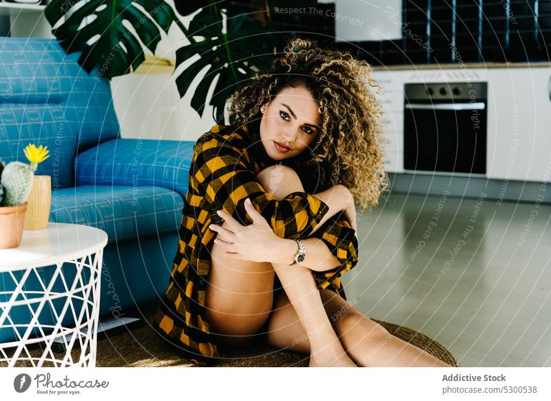 Alluring woman in checkered shirt looking at camera sensual model style sofa curly hair floor fashion portrait appearance female young comfort home relax casual