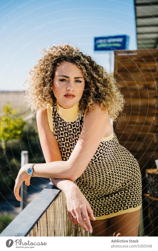 Attractive curly haired woman leaning on wooden railing balcony lean on blue sky cloudless sky sunlight summer charm attractive female young dress ornament