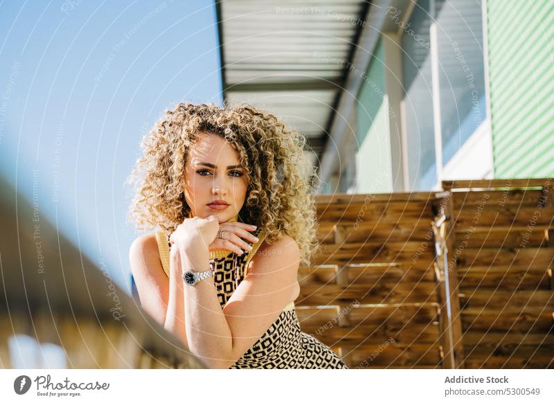 Attractive curly haired woman leaning on wooden railing balcony lean on blue sky cloudless sky sunlight summer charm attractive female young dress ornament