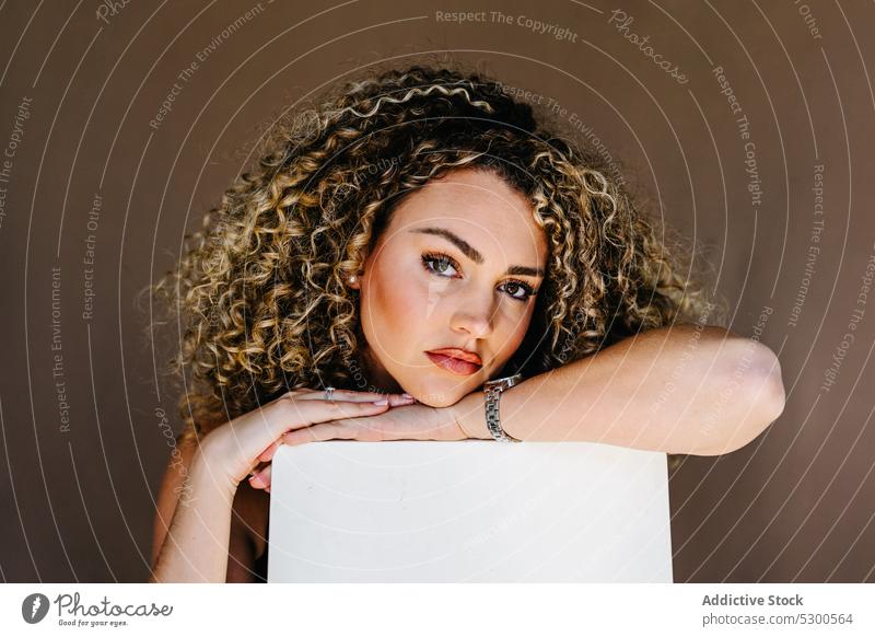 Young attractive woman leaning on white cube model studio shot portrait makeup appearance lean on curly hair individuality young unemotional emotionless female