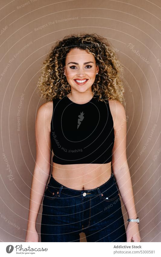 Smiling curly haired woman against brown background model toothy smile charm gorgeous gaze outfit appearance studio shot happy positive cheerful cosmetic female