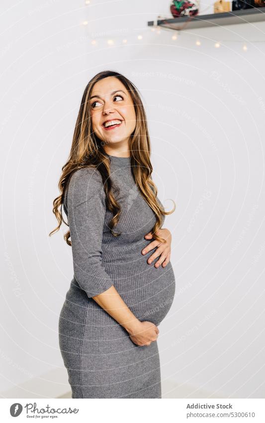 Happy pregnant woman touching belly touch belly garland glow await carry baby expect excited smile happy female young style dress prenatal pregnancy tummy