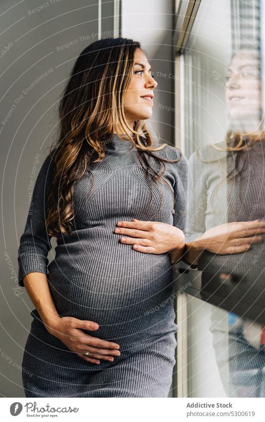 Pregnant woman standing near window caressing belly pregnant love touch belly maternity leave anticipate tranquil mother await smile female young stomach