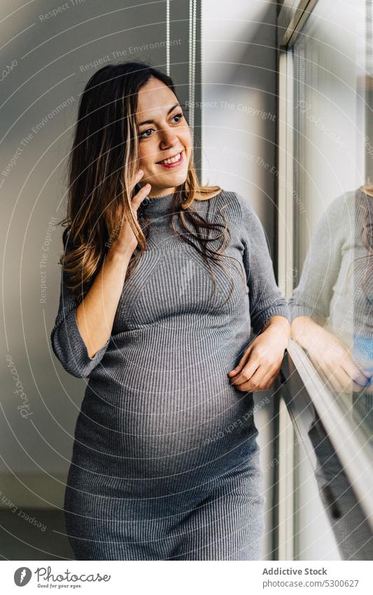 Smiling pregnant woman talking on cellphone using smartphone speak window phone call apartment conversation communicate positive smile female young