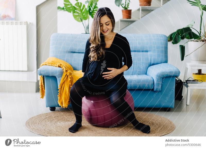Cheerful pregnant woman sitting on fit ball at home training exercise wellbeing touch belly maternity leave leisure healthy smile cheerful female young delight