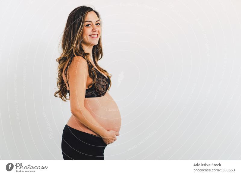 Young smiling woman carrying baby standing against white background pregnant studio shot happy maternity leave care smile love await glad caress touch belly