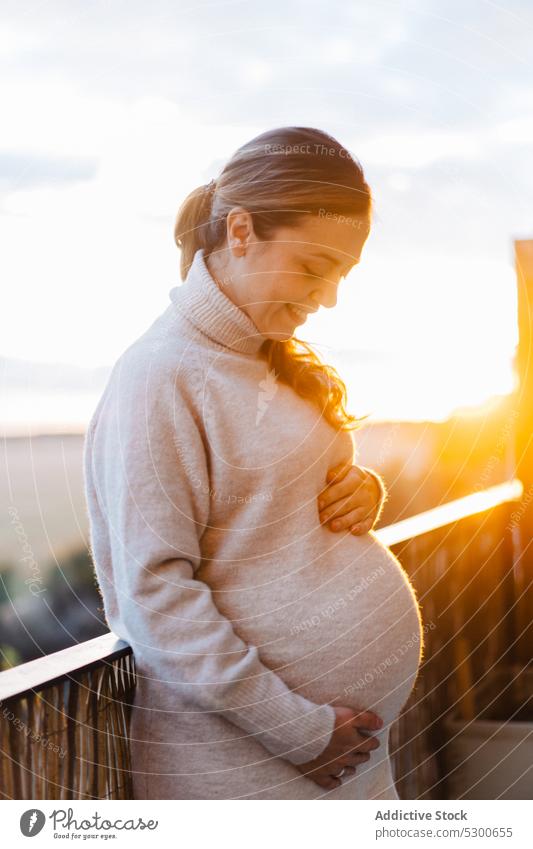Happy pregnant woman hugging belly on terrace unborn baby tender love caress touch belly sunlight smile happy female young ponytail anticipate maternity leave