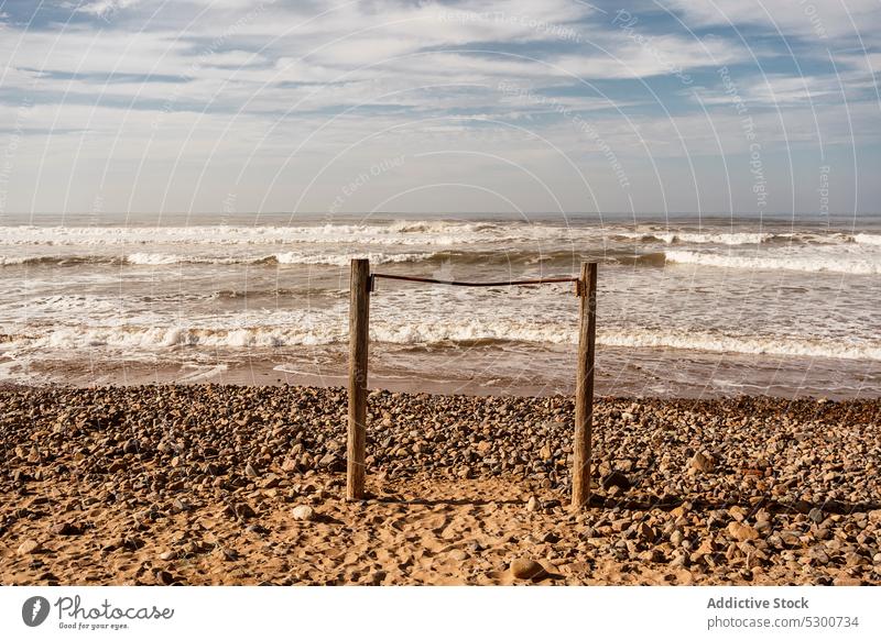 Sandy beach with wooden poles against wavy sea wave coast sand cloudy foam sky shore nature ocean mauritania sahara water scenic seashore seascape coastline