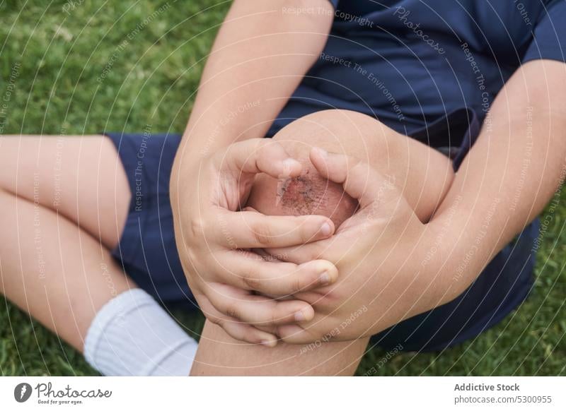 Boy sitting on grass after injury boy rest injure suffer pain ache sportswear hurt lawn athlete problem unhappy knee dissatisfied upset displease daytime
