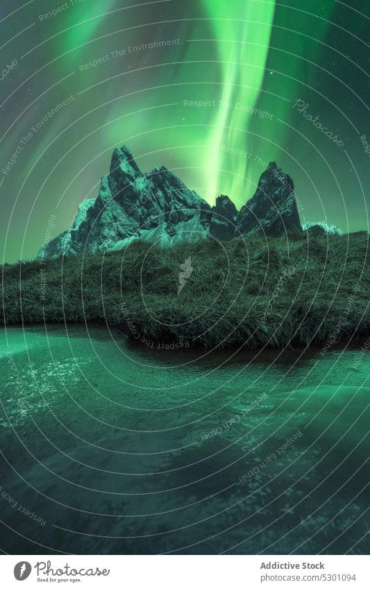 Scenic view of snowy mountains and lake under sky with polar light aurora borealis northern night Iceland Krossanesfjall Eystrahorn winter ridge green scenery