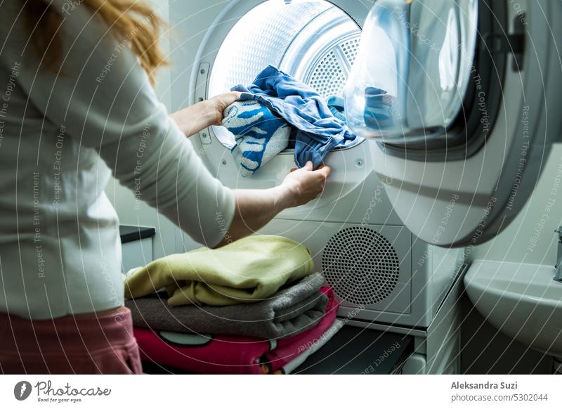 Woman doing laundry. Dryer machine in a Landry room at home drying clothes. Housewife unloading dryer and folding clean and dry linen. Household chores concept