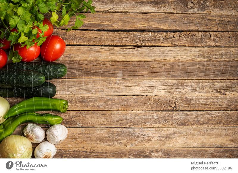 Vegetables to prepare gazpacho, tomato, cucumber, onion, garlic, peppers and parsley, on one side of the photo leaving space for copy on a rustic wooden background.
