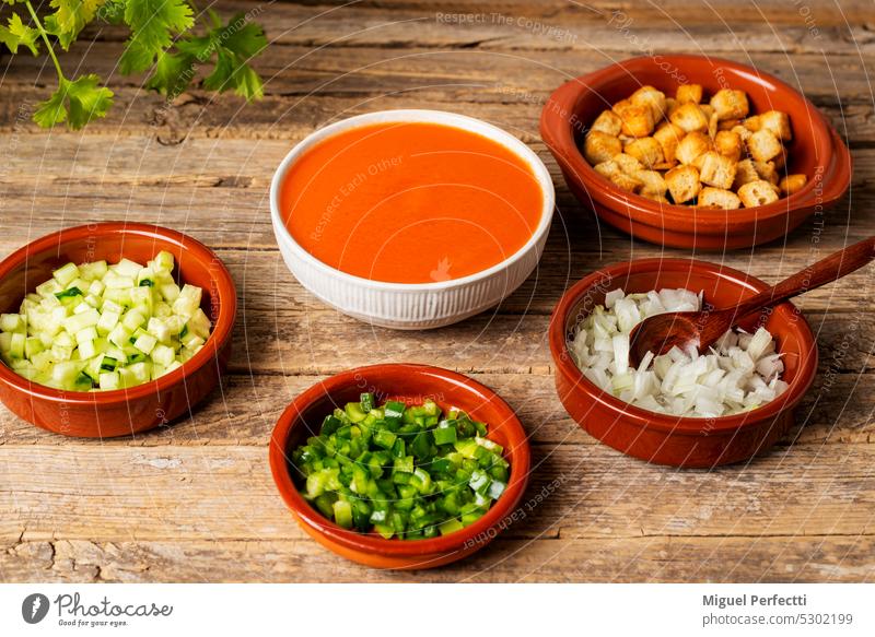Bowl with gazpacho next to some clay plates with chopped vegetables and fried bread to add to the gazpacho, on a rustic table. bowl ingredients fresh food