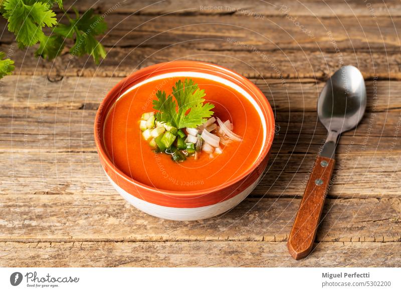 Bowl with gazpacho and pieces of vegetables, on an old and rustic wooden table, diner view. fresh chopped bowl healthy vegan food spanish mediterranean spoon
