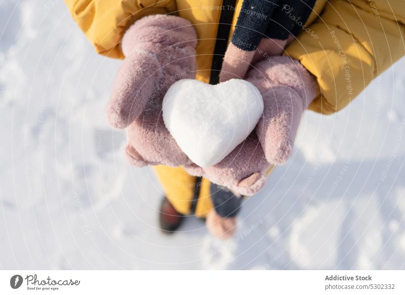 Anonymous person with heart shaped snowball in winter day show demonstrate cold frost nature warm clothes frozen wintertime ground season countryside weather