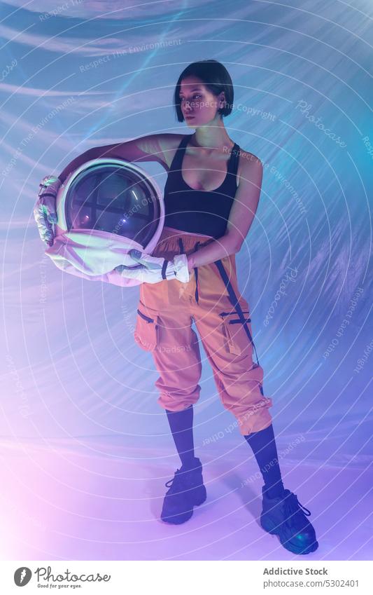 Confident woman with helmet in studio confident serious neon calm protect astronaut cosmonaut futuristic focus thoughtful female young unemotional light