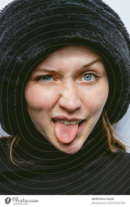 Positive woman in hat showing tongue portrait show tongue expressive funny grimace make face happy tongue out female young positive joy cheerful playful