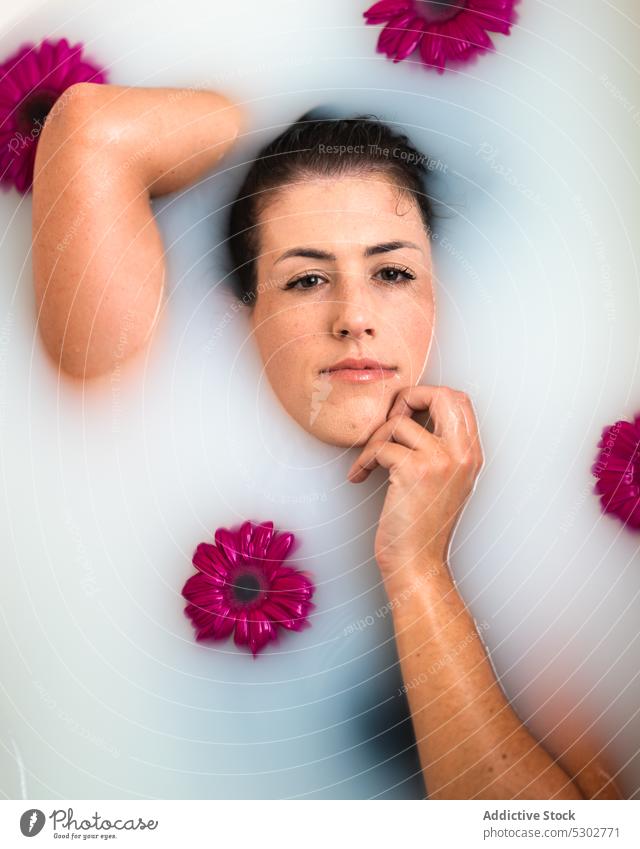 Tender woman touching face while relaxing in bathtub with flowers and milk touch face spa sensual wellness therapy female wet hair healthy tranquil harmony