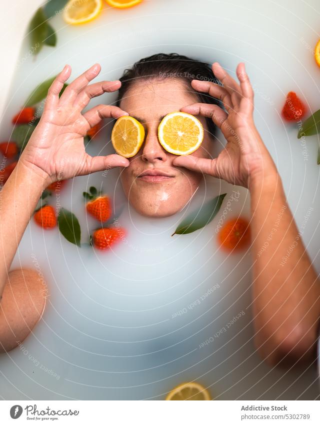Woman covering eyes with oranges in bathtub woman cover eyes slice milk strawberry leaf body care recreation funny creative female wellness spa routine at home