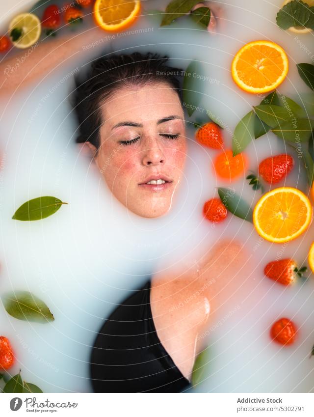 Relaxed woman taking bath with fruits and berries at home orange slice milk leaf calm strawberry spa procedure female leisure healthy therapy treat peaceful