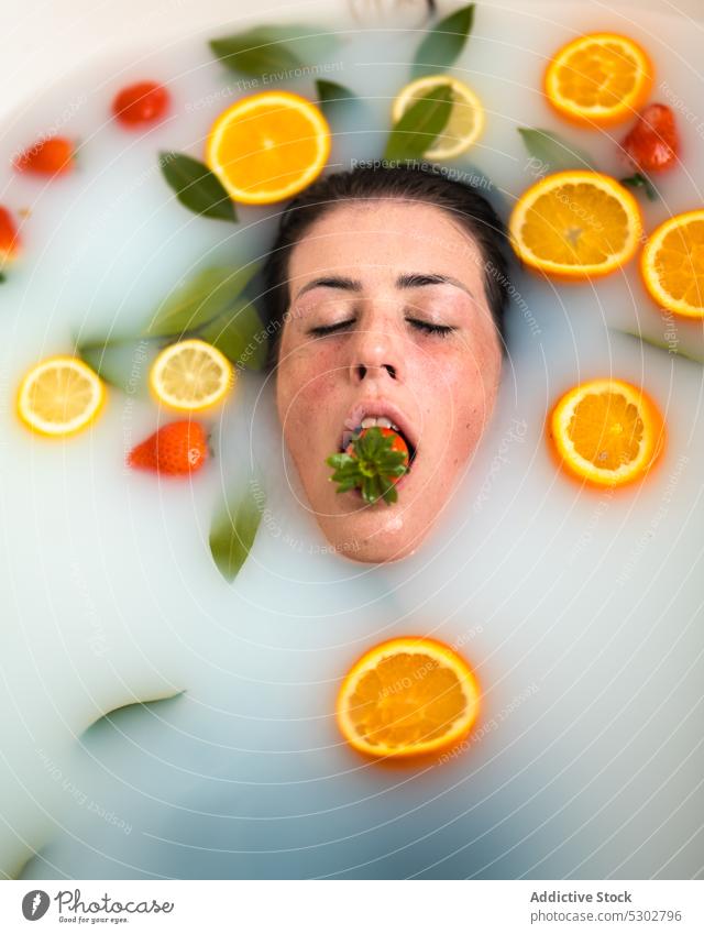 Woman taking bath with strawberry in mouth woman citrus orange slice milk eat wet hair spa female healthy rejuvenate procedure bathroom body care fruit water