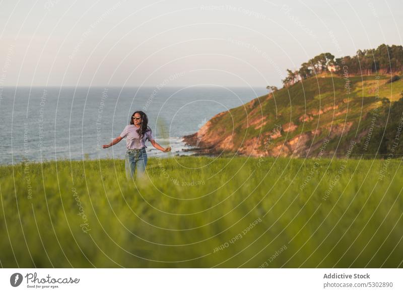 Happy woman running on grassy hill near sea walk admire nature picturesque peaceful travel smile happy female casual sunglasses enjoy summer young freedom trip