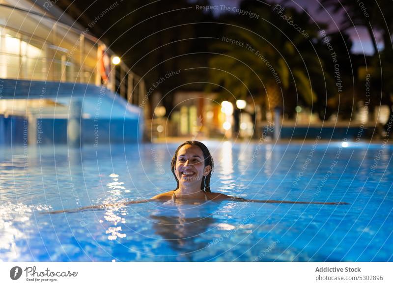 Cheerful woman swimming in pool at resort happy cheerful vacation smile enjoy night water chill female young rest poolside relax summer recreation positive