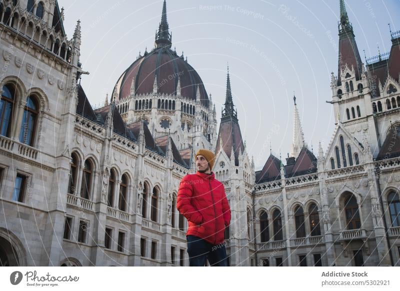 Young man standing by classic building tourism historic architecture hungarian parliament building tourist street confident young male vacation sightseeing