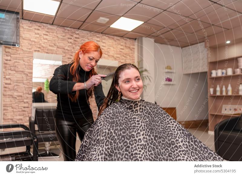 Cheerful hairdresser combing hair of client women brush hairstyle salon hairdo beauty procedure smile customer professional master positive female work job