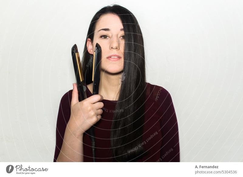 Young woman with long hair holding a hair straightener on a white background. Concept of using heat to straighten hair. iron hair hair iron treatment