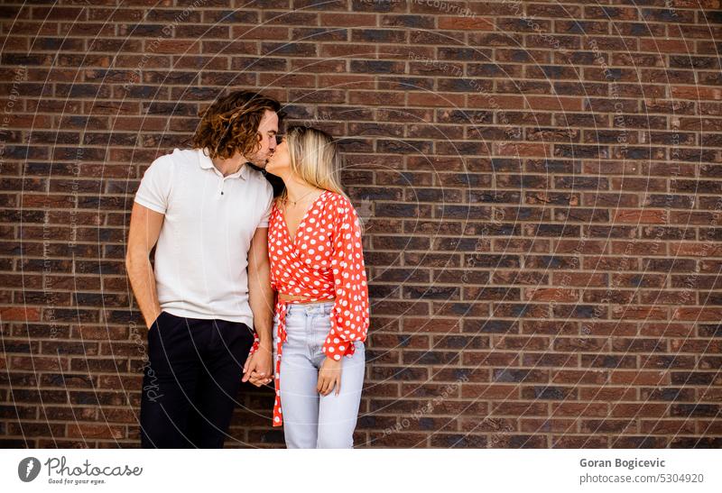 Smiling young couple in love in front of house brick wall adult beautiful casual caucasian cheerful cute facade female happiness happy home lifestyle man new