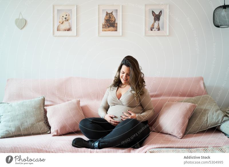 Positive pregnant woman relaxing on sofa belly maternal expect touch happy pregnancy smile comfort home tummy anticipate female couch await motherhood stomach