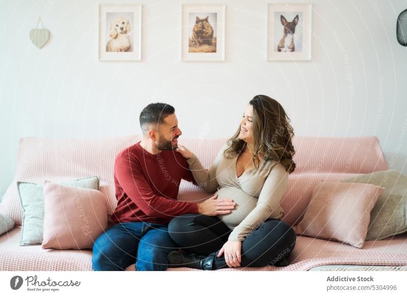 Happy man with pregnant woman on sofa couple love relationship happy together bonding home affection couch fondness expect husband wife smile belly tummy