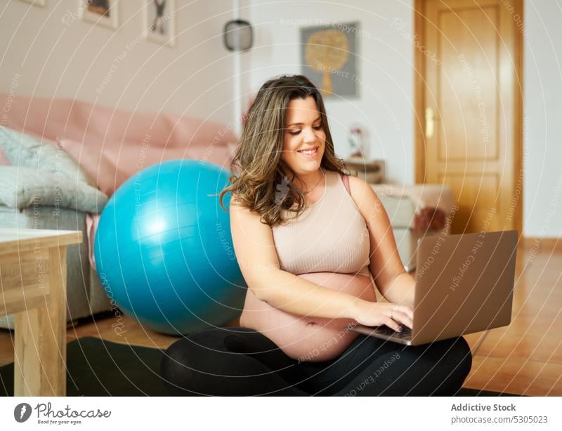 Happy pregnant woman using laptop while training smile happy fitness fit ball break typing cheerful female belly long hair sportswear pause positive pregnancy