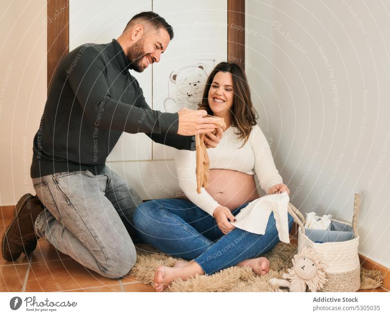 Joyful expecting couple looking at baby clothes wife husband pregnant belly maternal nursery smile glad pregnancy await childbearing prenatal motherhood