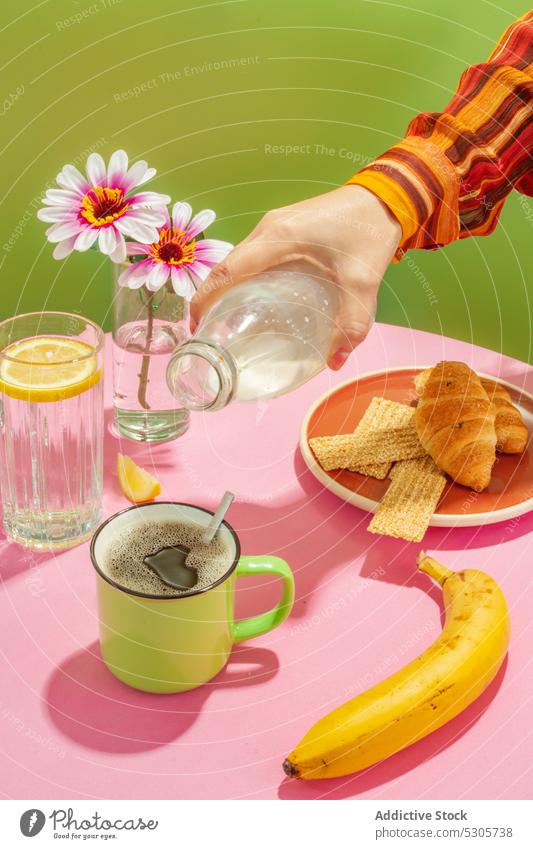 Crop person pouring milk into cup of coffee breakfast croissant beverage morning flower banana delicious cream fresh tasty drink vase sweet table pastry yummy