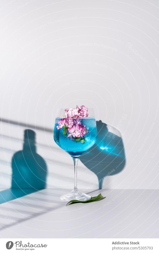 Refreshing cocktail with ice cubes near flowers and bottle drink beverage blue glass alcohol refreshment cold liquid shadow table aperitif bloom delicious serve