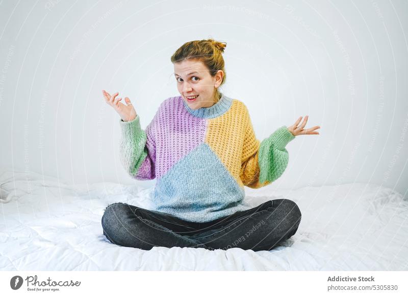 Confused woman in lotus pose on bed puzzle confuse outfit home bedroom sweater knitted casual young colorful style jeans female legs crossed padmasana