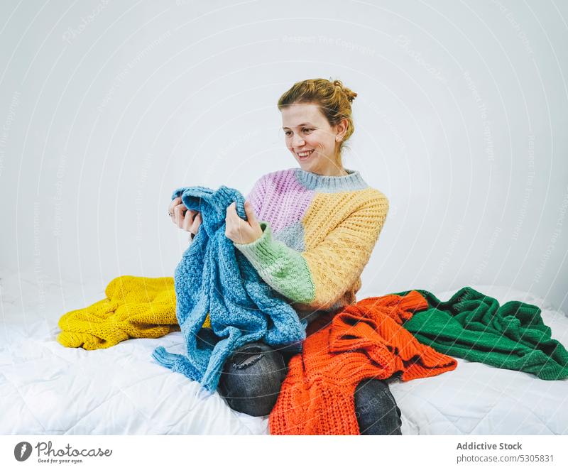 Cheerful woman choosing sweater on bed choose smile comfort positive happy cheerful home cozy young bedroom female soft apartment joy content warm clothes