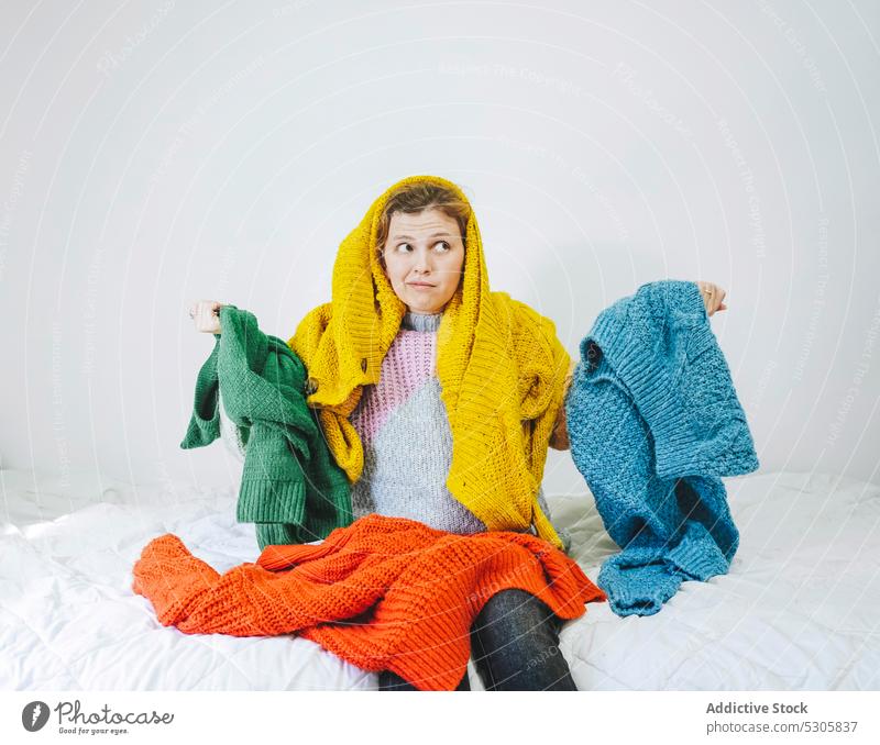 Puzzled woman with colorful sweaters looking away choose book bed confuse home comfort casual pensive thoughtful knitwear cloth young bedroom female