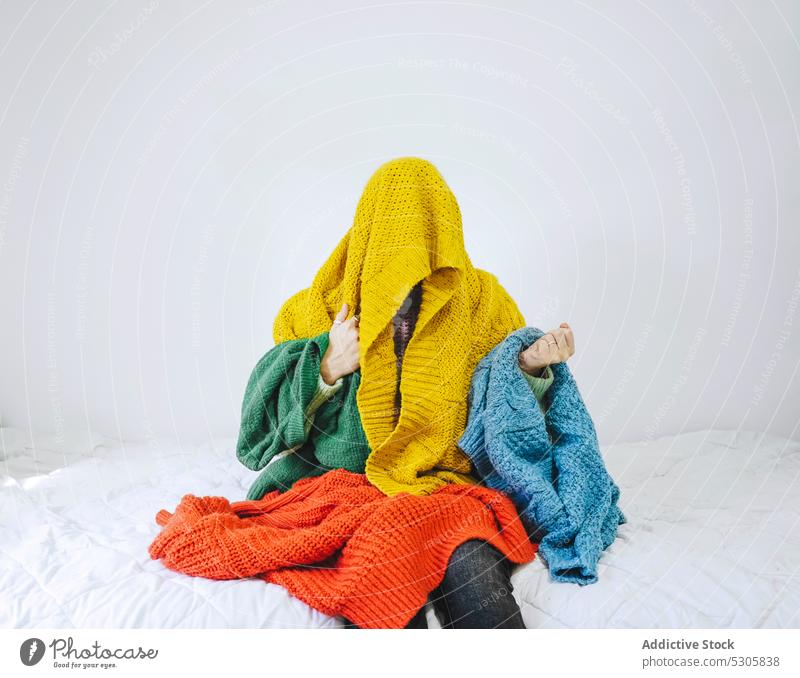 Anonymous woman covered with colorful sweater choose book bed confuse home comfort casual pensive thoughtful knitwear cloth young bedroom female warm clothes