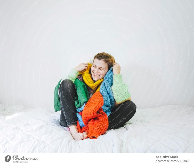Cheerful woman with colorful sweaters on bed rest home positive comfort smile cheerful happy cozy relax female eyes closed young knitted bedroom jeans style