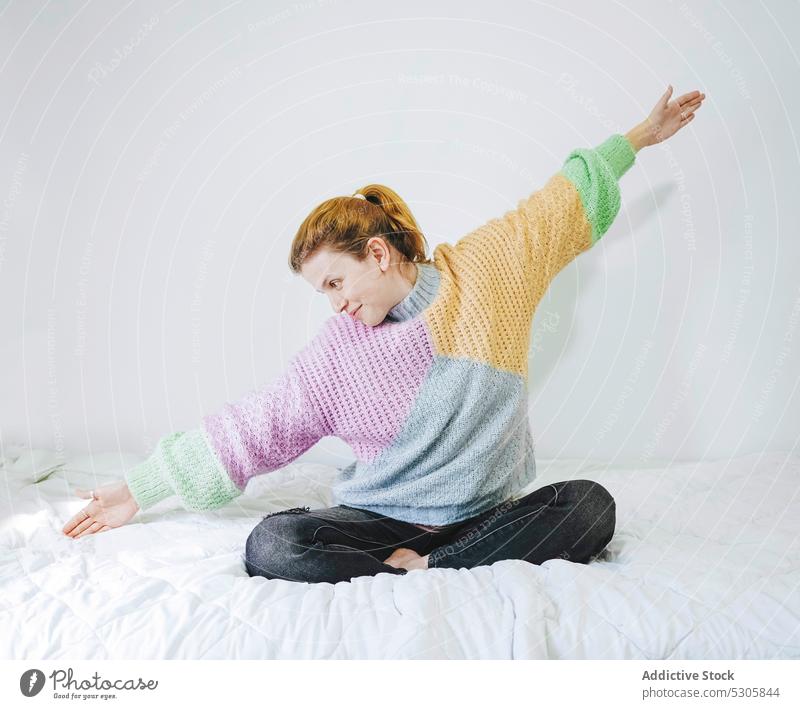 Content woman stretching on bed lotus pose morning home calm relax meditate padmasana peaceful young female comfort yoga rest bedroom colorful casual apartment