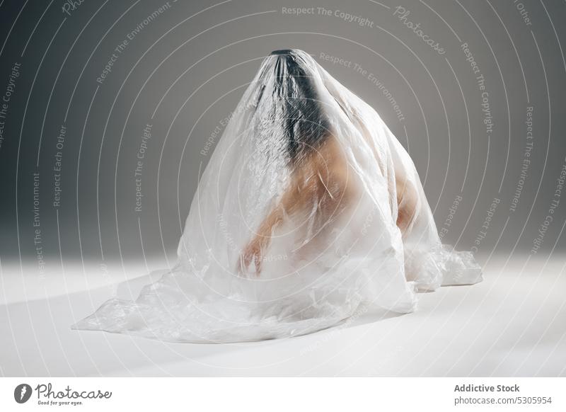 Anonymous woman wrapped in polyethylene sitting on floor naked nude anonymous pollute disaster environment ecology rubbish cellophane female helpless concept